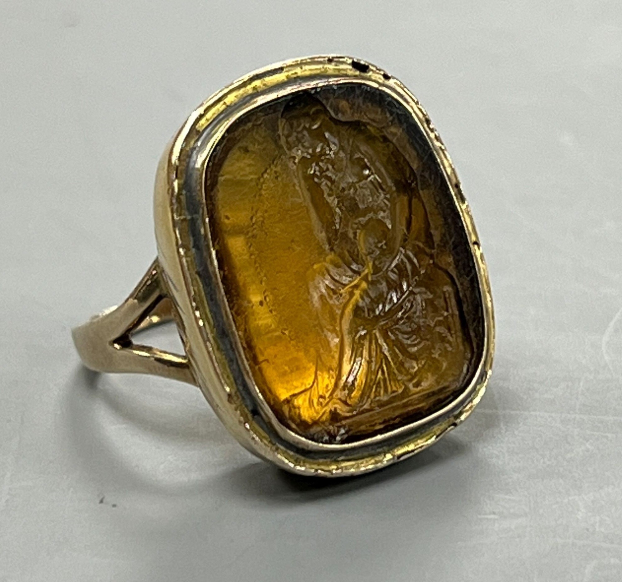 A 19th century yellow metal and intaglio yellow paste set ring, carved with 'The Thinker' after Rodin, size I, gross 8.7 grams.